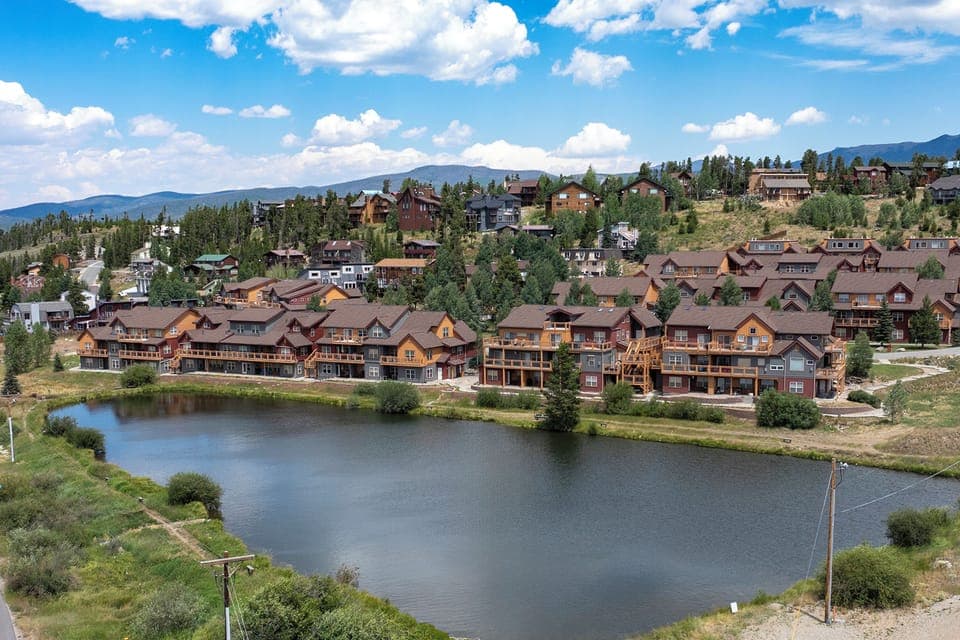 Mountain resort community featuring lakeside lodges and alpine-style buildings surrounded by forest and peaks.