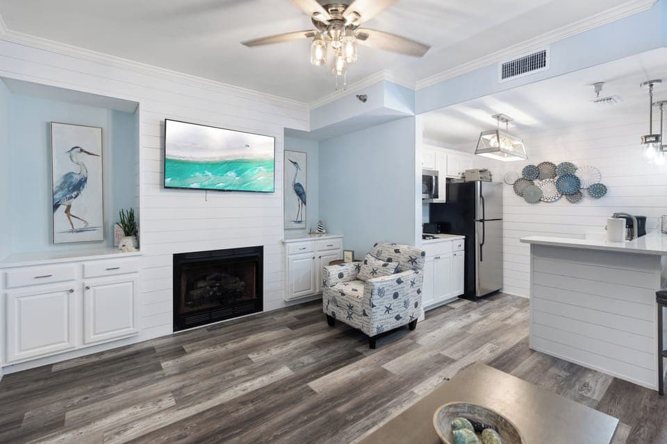 Unwind in your coastal-inspired living space featuring a cozy fireplace and modern kitchen perfect for preparing meals during your stay.