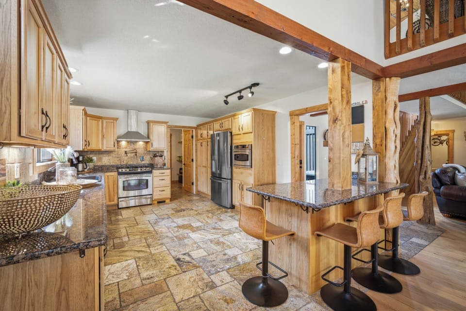 You'll love gathering in this spacious kitchen featuring warm wood cabinets, granite counters, and rustic exposed beams that create a cozy mountain retreat atmosphere.