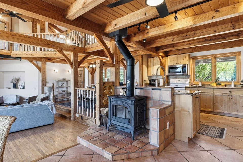 A warm, open-concept living space anchored by a wood-burning stove and rich timber beams—perfect for cozy nights in.