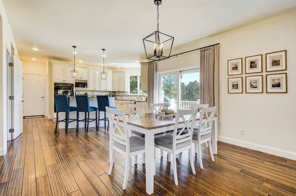 The dining area flows seamlessly into the kitchen, where white cabinetry and navy blue island seating add a crisp contrast against the warm hardwood-style floors and the natural light streaming through the windows.