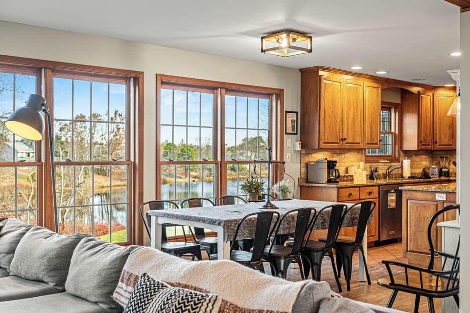 Cozy open living‑dining space with warm wood accents, soft neutrals, and sunlight streaming through wide windows. (Laker's Pointe)
