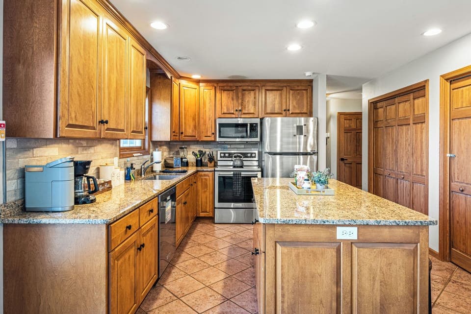 Warm wood‑toned kitchen with granite counters, stainless steel appliances, and a neatly organized island centerpiece. (Laker's Pointe)