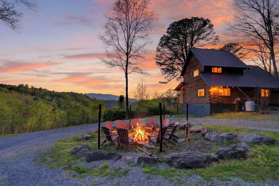 Hillside cabin with a glowing fire pit and Adirondack chairs, set against a colorful mountain sunset. (Isaiah's Cabin)
