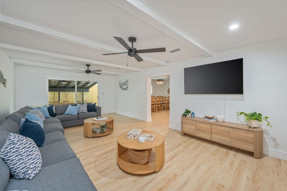 Bright, spacious living area with a cozy sectional, large TV, and open flow to the dining space and patio.
