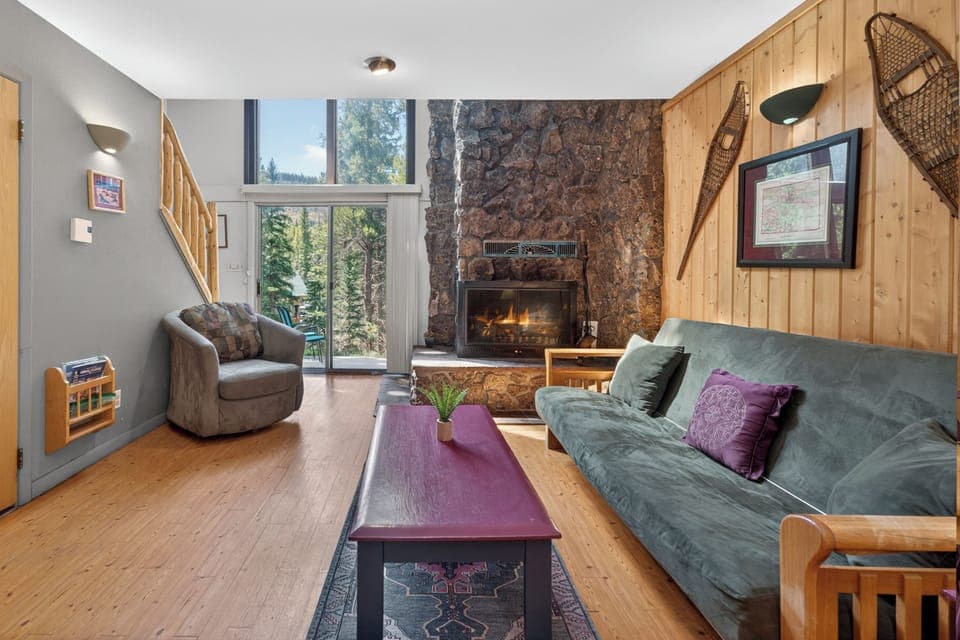 Picture yourself unwinding in this cozy living room, where a stone fireplace and forest views create the perfect mountain retreat after a day of adventure.