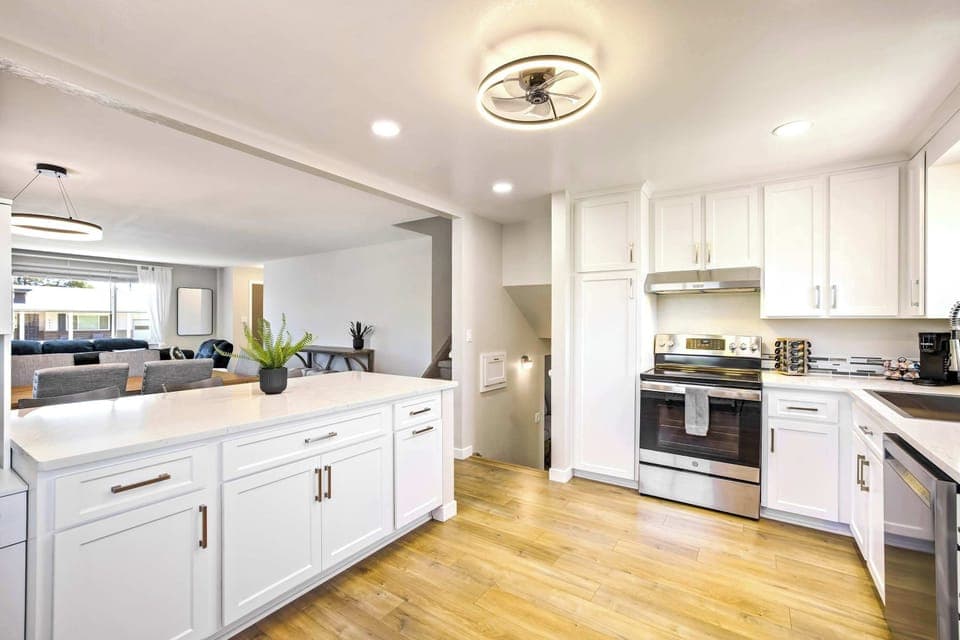 The kitchen runs long and bright with white shaker cabinets, stainless appliances, and warm wood floors that carry through from the main level. A flush ceiling light and recessed lighting keep the workspace well lit from every angle.

