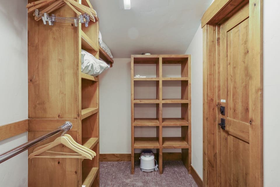 Wooden walk-in closet with shelves, hanging rods, and hangers.
