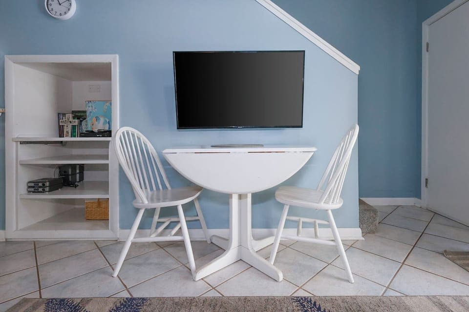 This cozy nook features a wall-mounted TV and a charming round table with two white chairs, perfect for meals or games