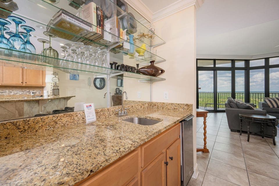 Kitchen area wet bar with granite countertops and a cozy living area showcasing expansive views through large windows