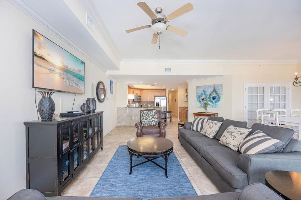 Inviting living room featuring a large TV, comfortable seating, queen sofa-sleeper, and a view into the modern kitchen area