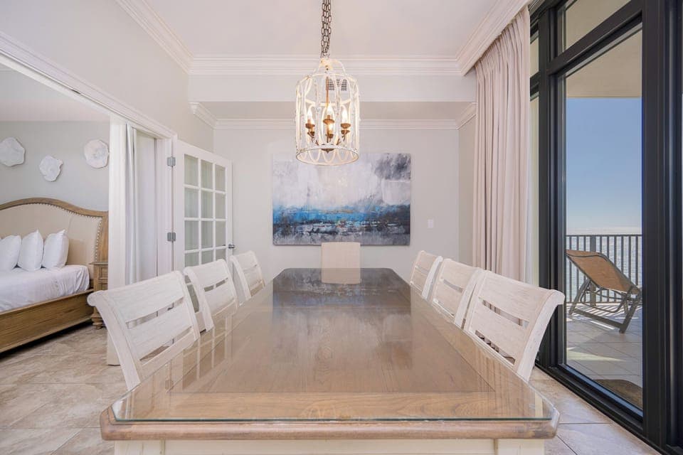Dining area featuring a large table, elegant chandelier, and a stunning view of the coastline through glass doors
