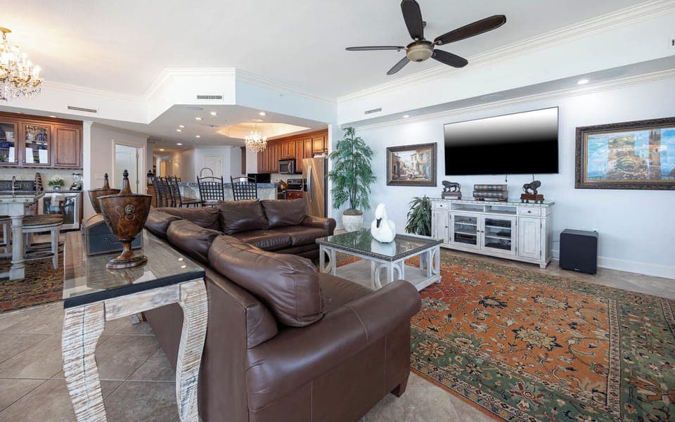 This living area features a cozy brown leather sofa, a large TV, and a stylish coffee table on a vibrant area rug
