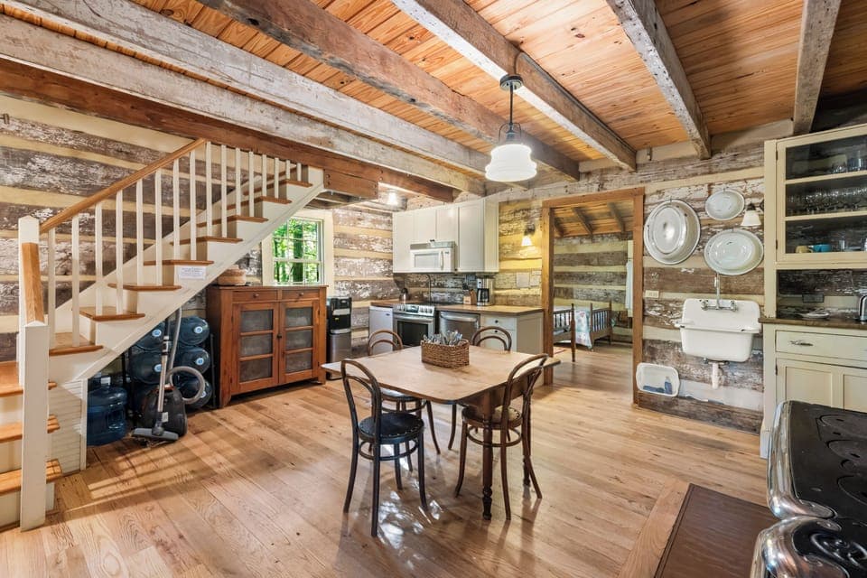 Charming farmhouse-style kitchen with cream cabinets, a vintage sink, glass-front cabinetry, and rustic log walls—blending comfort with classic cabin character.