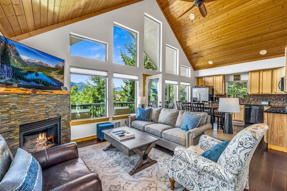 Vaulted living room with soaring windows, stone fireplace, and panoramic mountain light