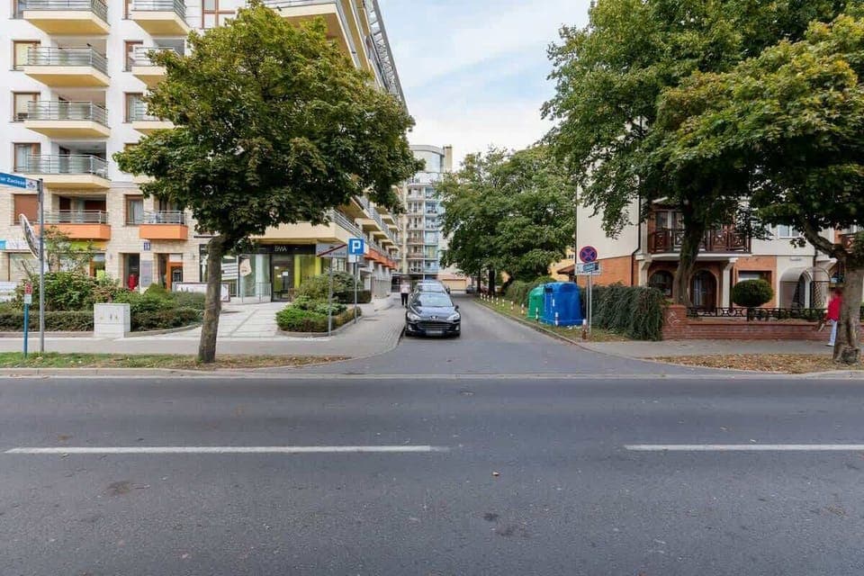 A street view outside the apartment, showing neighboring buildings, trees, and a few cars parked along the road.
