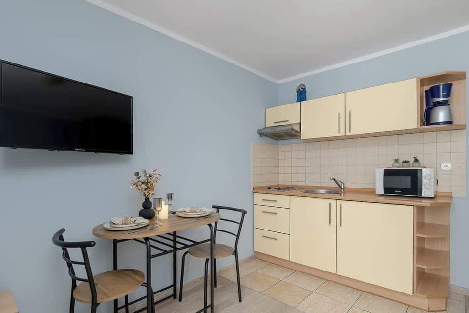 The living space features a small table with chairs, creating a spot for dining or working. A large TV hangs on the wall for entertainment.