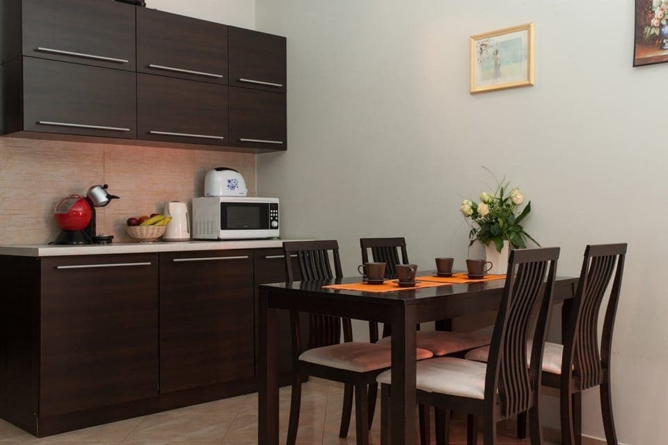 A compact kitchen area with dark wood cabinets, featuring basic appliances such as a microwave and a coffee maker. A small dining table with chairs is neatly arranged beside it.