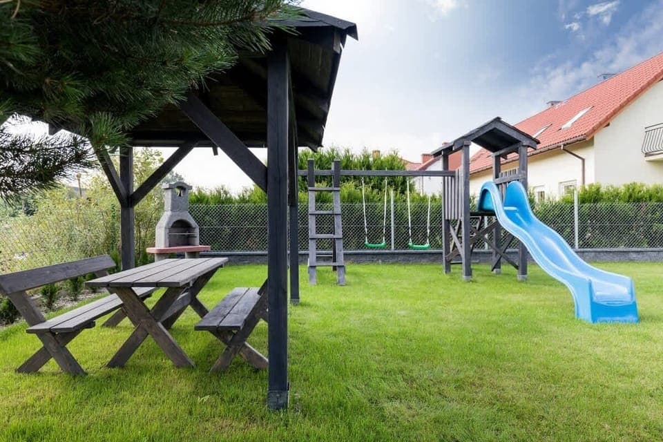 An outdoor area with a wooden gazebo, a picnic table, and a playground set, perfect for family gatherings and outdoor play.