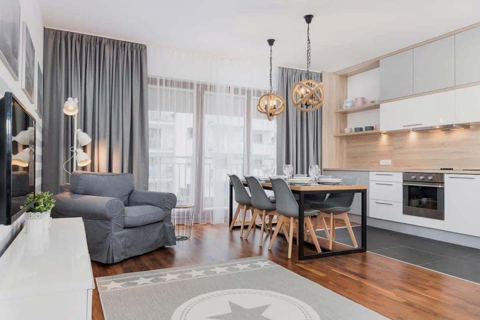 Bright, spacious living room with kitchenette. The grey long curtains bring a lot of cosiness and the soft grey armchair provides a relaxing and restful environment. Dining table for 6 people. 