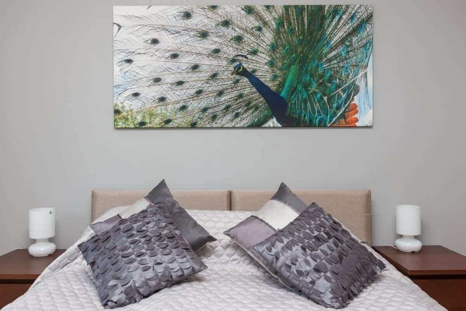 Similar to the previous one, but this room has different angles showing more of the headboard and bedside tables. The artwork and decorations appear the same.