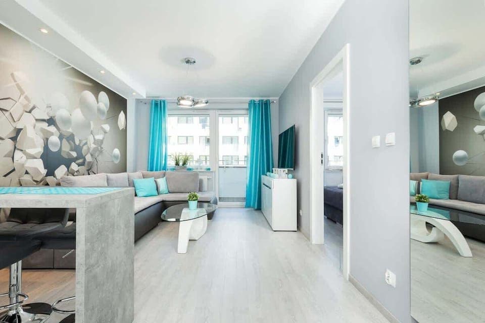 A living room with a modern gray sofa, large windows bringing in natural light, and decorative elements on the walls, creating a comfortable and stylish space.