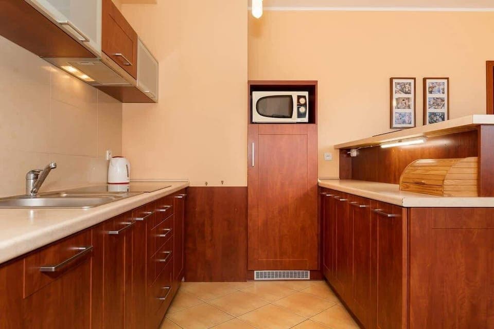 A traditional kitchen setup with rich wooden cabinets, a beige backsplash, and plenty of counter space. There’s a microwave and other appliances, creating a functional cooking area.