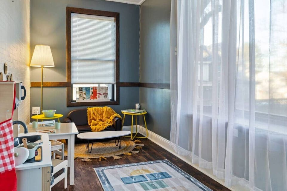 Bright, Playful, and Just Their Size – This inviting corner features a child-sized leather loveseat, vibrant yellow accents, and sheer curtains that catch the sunlight just right.