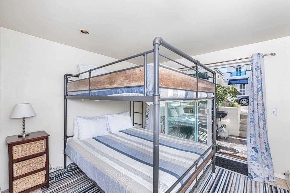 Lower level bedroom provides Queen over Queen bunk bed, linens, TV, closet, sliding glass door out to front sub-street patio and seating.
                