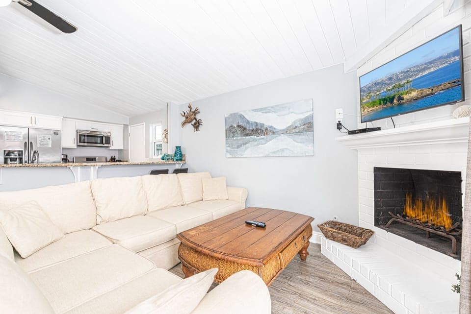 The living area includes sofa, cable TV, dining table with seating for 6, and kitchen beyond.
                