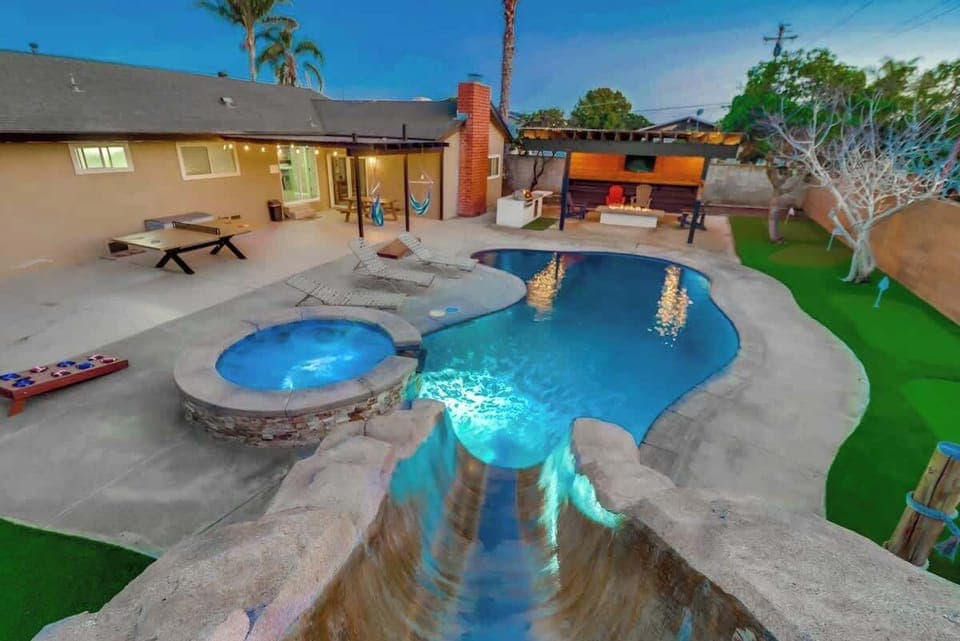 Pool lights illuminate the hot tub and base of the slide