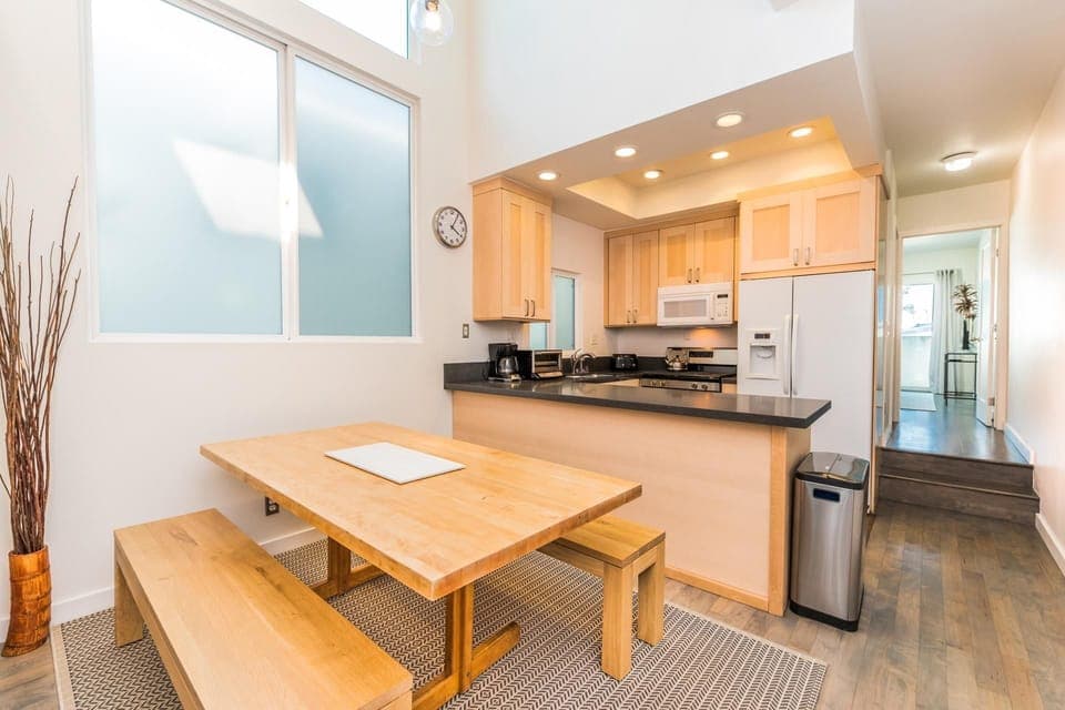 Dining table with bench seating sits adjacent to the kitchen on one side and the central staircase on the other. Located on middle (main level).
                