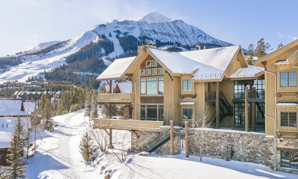 Mountain chalet nestled in pristine snow with dramatic alpine peaks rising behind the property.