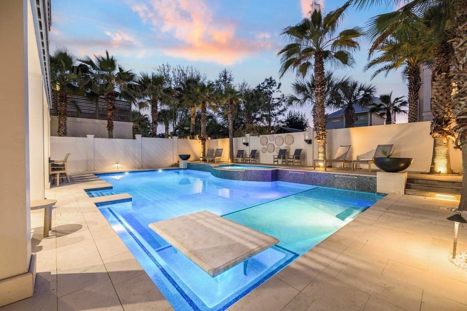 Dive into your private oasis with this stunning illuminated pool, surrounded by tropical palms and elegant lounging areas for perfect evening relaxation.