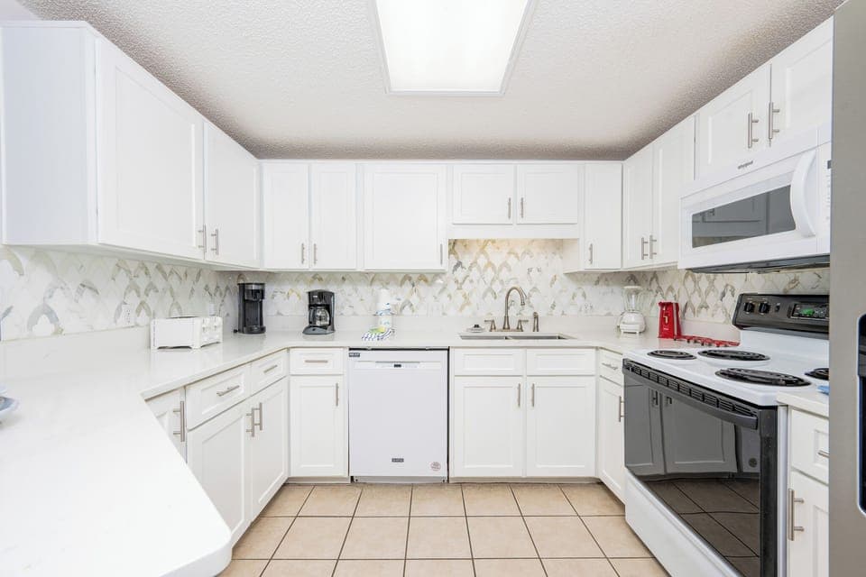 Prepare meals in this stylish kitchen featuring sleek countertops, ample storage, and white appliances for your convenience