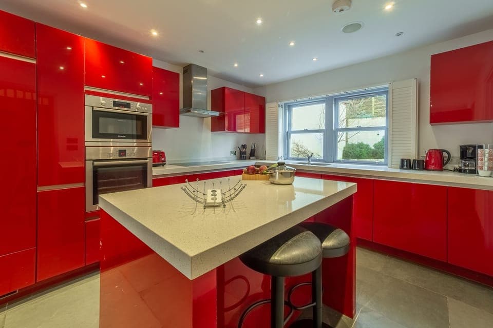 Spring Tide, Porthtowan. Ground floor: Dining kitchen with high gloss red units, a double oven and hob, dishwasher, fridge/freezer and washing machine. Central island with breakfast bar. Dining area with seating for eight guests