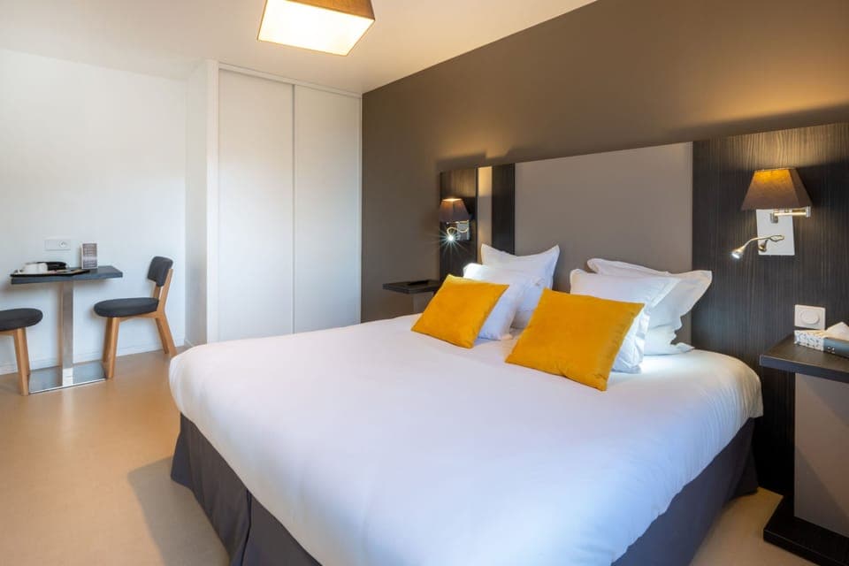 The cozy studio features a plush double bed adorned with vibrant yellow cushions, complemented by sleek bedside lamps that softly illuminate the modern décor in warm tones.