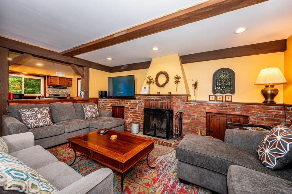 Living room centered on a red brick fireplace with a wood mantel, flanked by gray upholstered sofas and a wooden coffee table.