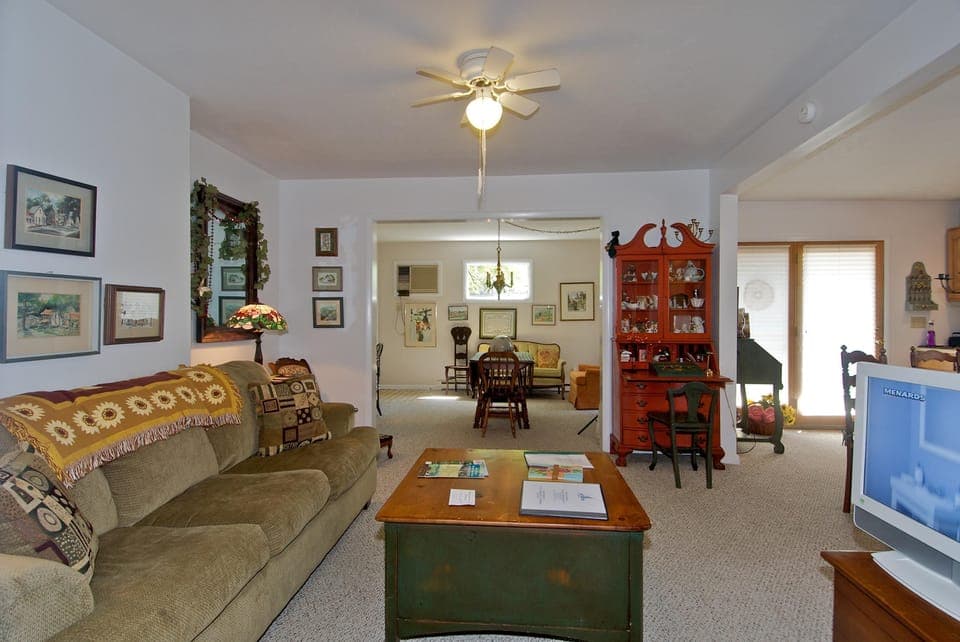 Living room with olive-green sofa, vintage floral throw, green wooden coffee table, and red display cabinet.