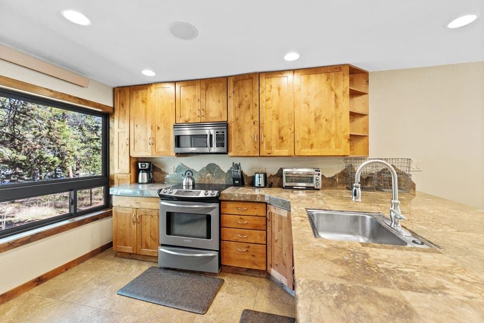 Full kitchen with stainless steel appliances, breakfast bar with seating for three, and a wine cooler.