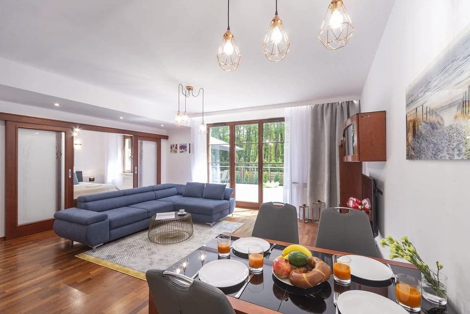 Living room with a different perspective, showing the sofa and more of the dining space. Warm wooden flooring complements the design.