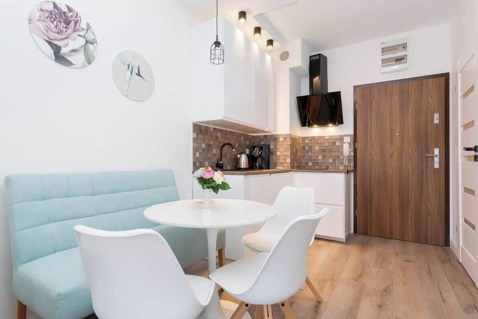 A stylish dining space with a round white table, contemporary chairs, and light wood flooring. The open-concept design connects to the kitchen and living room for a spacious feel.
