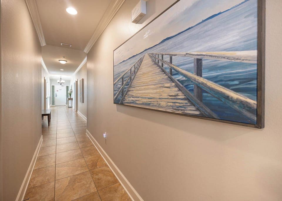 This hallway features a serene coastal painting, warm tile flooring, and leads to inviting spaces beyond