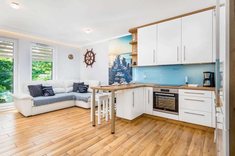 A spacious living room with a dining table and an open kitchen, featuring white cabinets and wooden flooring.