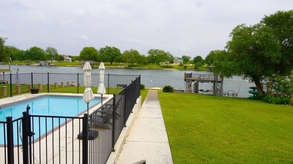 View of pool, yard, dock, and lake from back porch. 