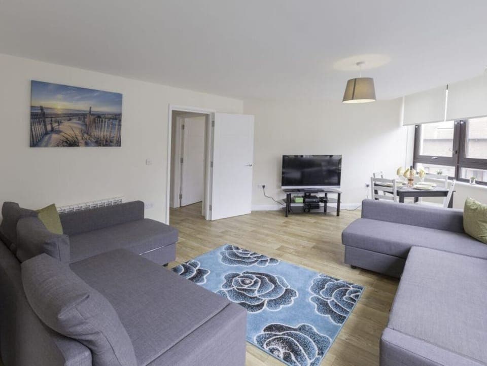 Living room with large grey sofa, blue patterned rug, wall art, and dining nook – Castle 6 - Southampton