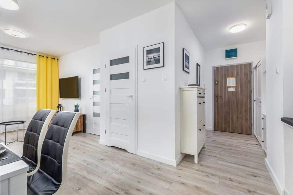 Liiving room shot showing a long hallway leading to other rooms, decorated with bright yellow curtains and simple furnishings.