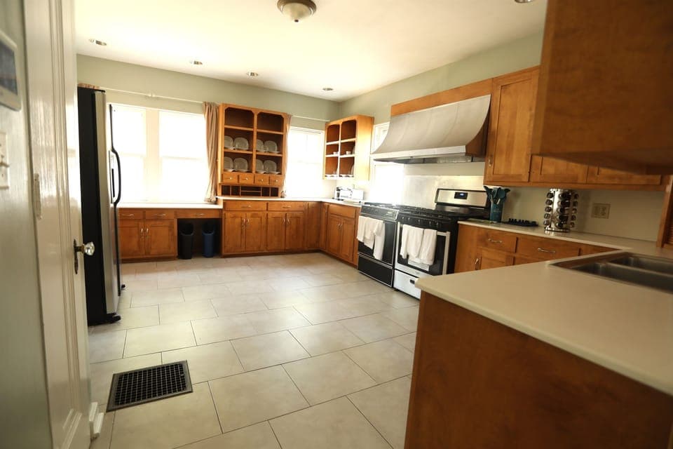 Kitchen shown with back to the Dining Room. The ADT panel and pantry are on the left. Four windows bathe the Kitchen in natural light arrested only by three sheer curtains and a set of blinds.