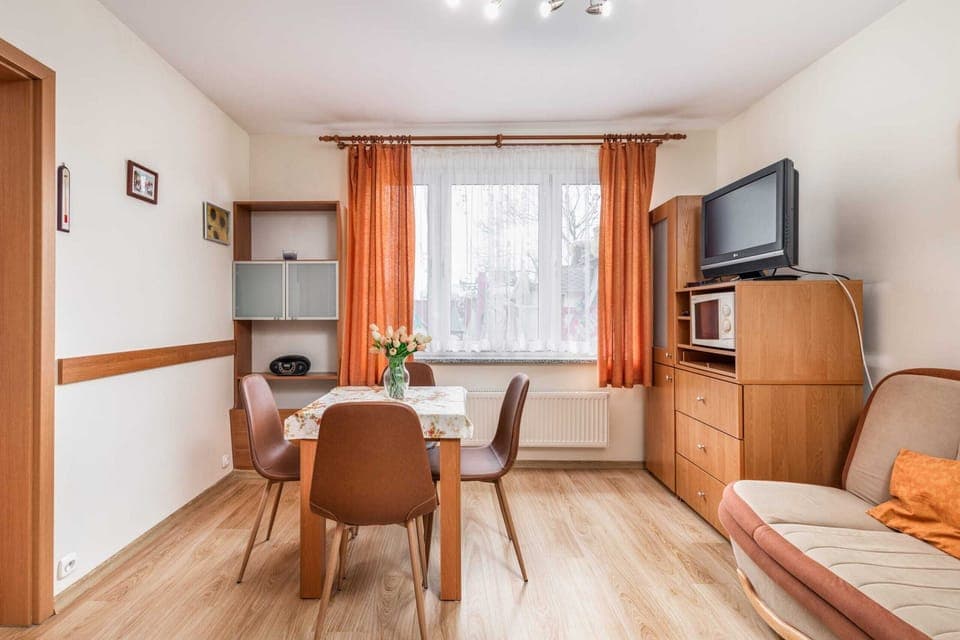 A spacious main area with a dining table, chairs, and a large window that fills the room with natural light. A TV is positioned for easy viewing from the dining area.