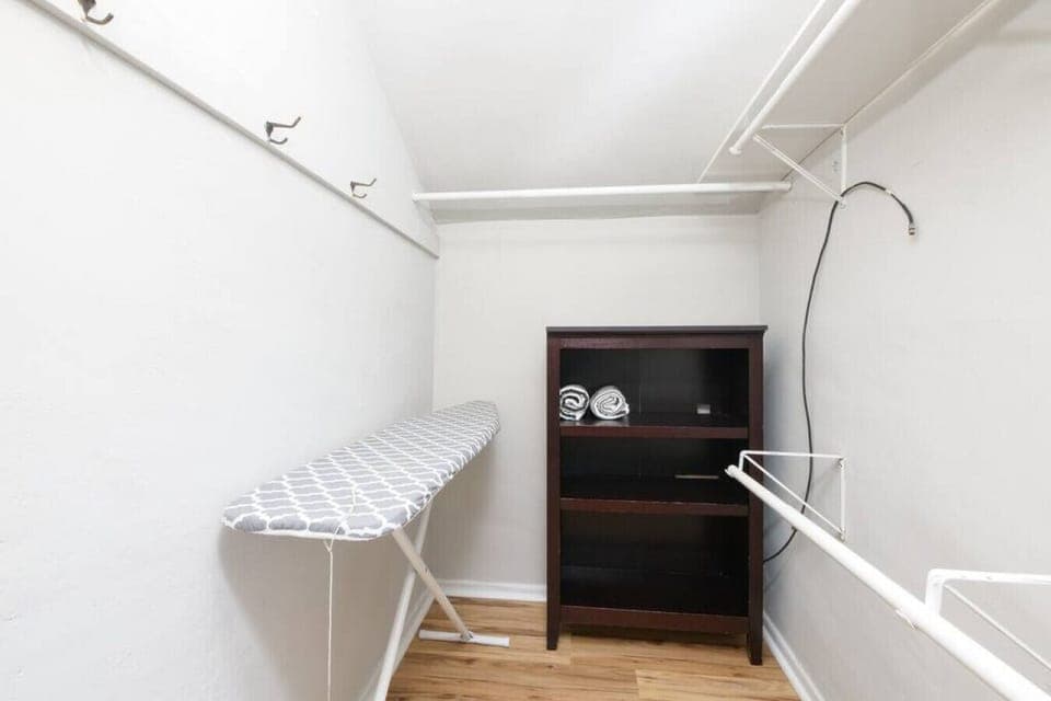Spacious walk-in closet with multiple shelves for storage   - Convenient ironing board included for guest use   - Organized layout with hooks and hanging racks for clothes